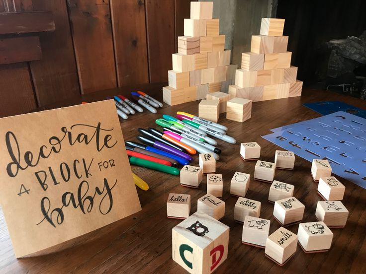 a wooden table topped with lots of blocks and dices next to a sign that says decorate a block for baby