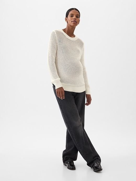 a woman standing in front of a white background wearing black jeans and a white sweater