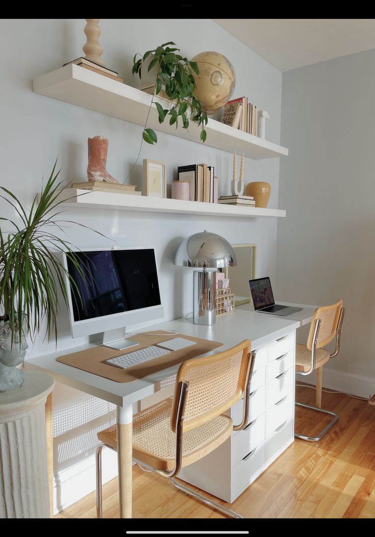 a desk with a computer on top of it next to two chairs and a potted plant