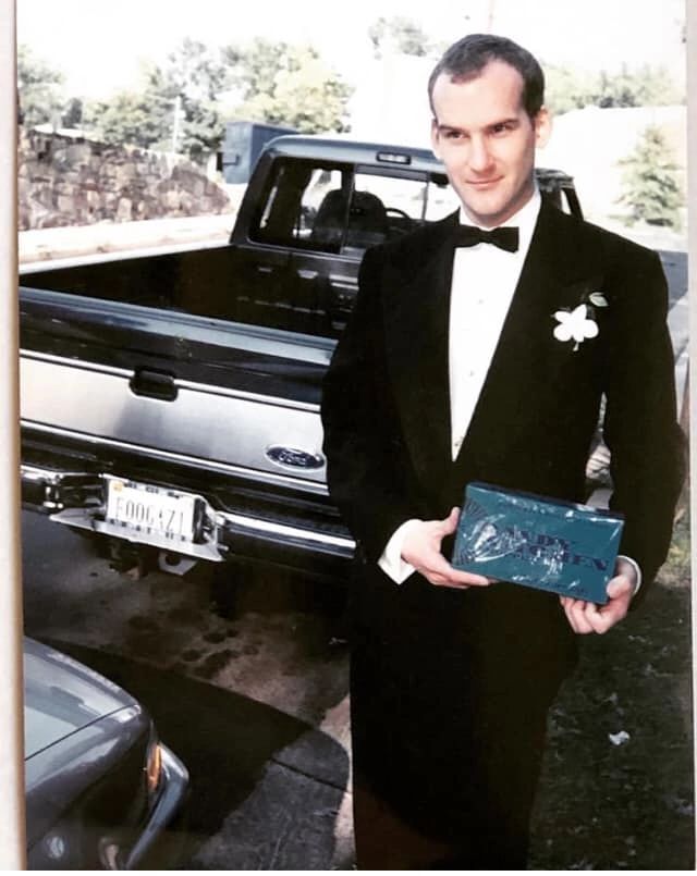 a man in a tuxedo standing next to a pickup truck holding a plaque