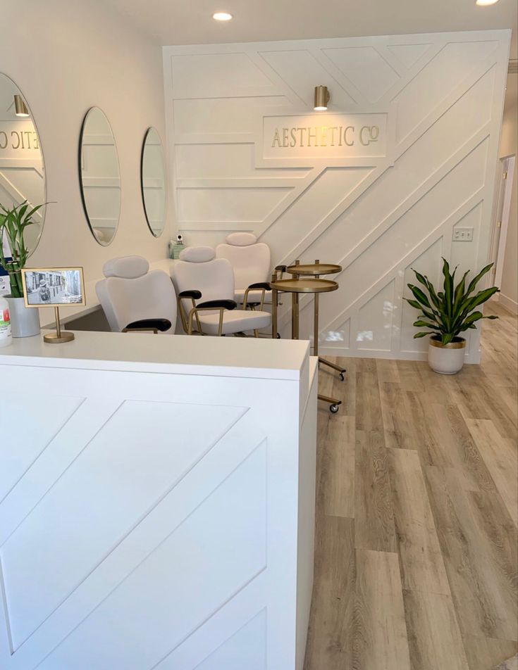 the interior of a hair salon with chairs and mirrors on the wall, potted plants in front of the counter