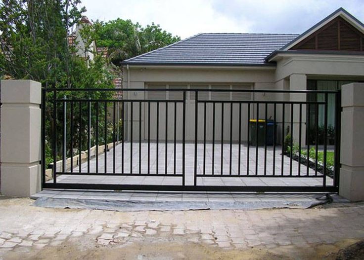 a gated driveway in front of a house with an iron fence and brick walkway