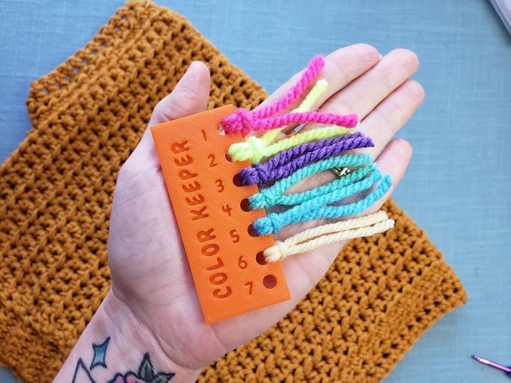 a person's hand holding an orange piece of string with colorful beads on it