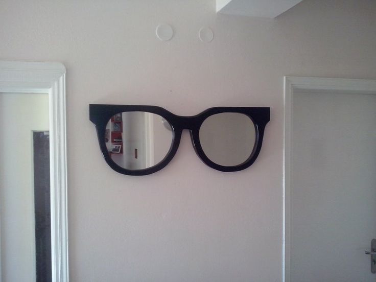 a pair of black glasses hanging on the wall next to a mirror that is reflecting it's reflection