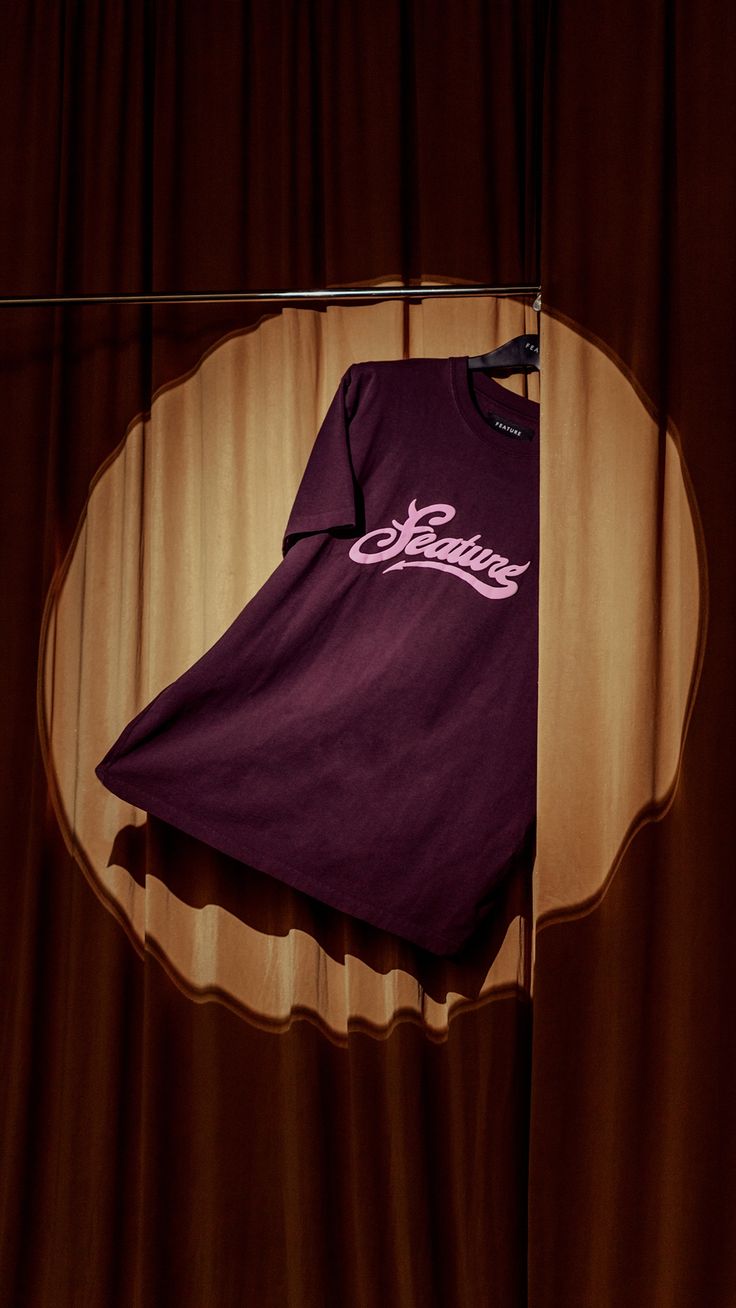 a t - shirt is hanging on a clothesline in front of a brown curtain