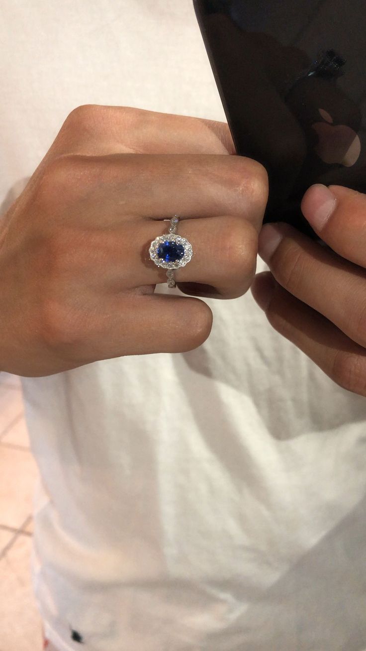 a woman is holding her cell phone and wearing a ring with an oval blue stone