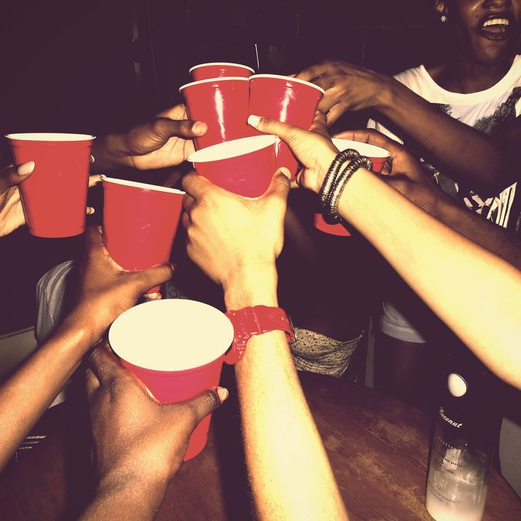 a group of people holding red cups in the middle of their hands, all around one another