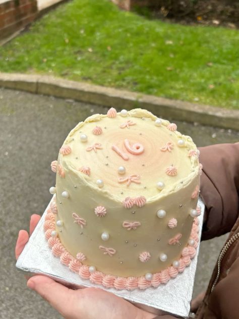 a person holding a cake in their hand on the street with grass and trees in the background