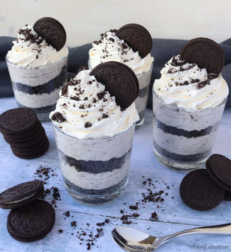 four desserts with oreo cookies and cream in them on a blue tablecloth