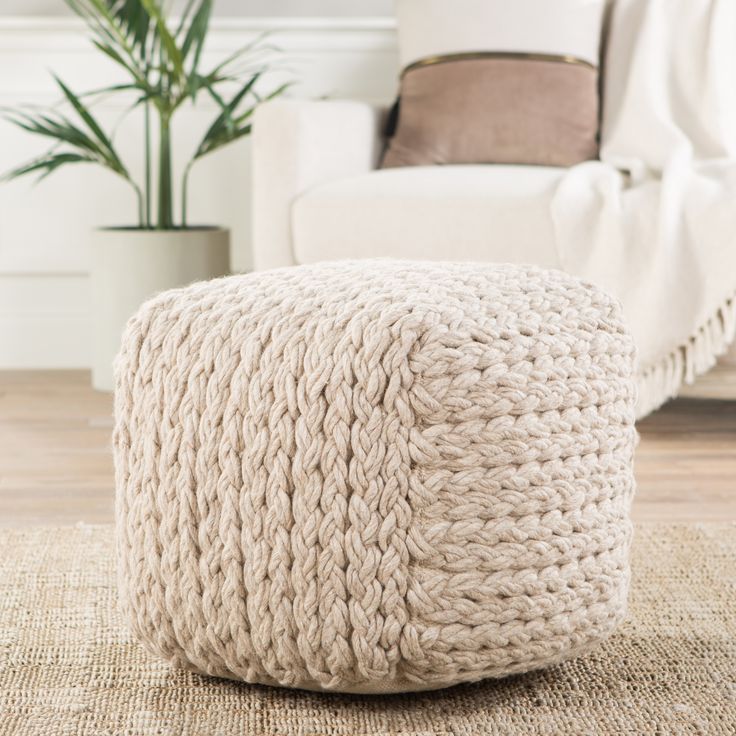 a knitted ottoman sits on the floor in front of a white chair and potted plant