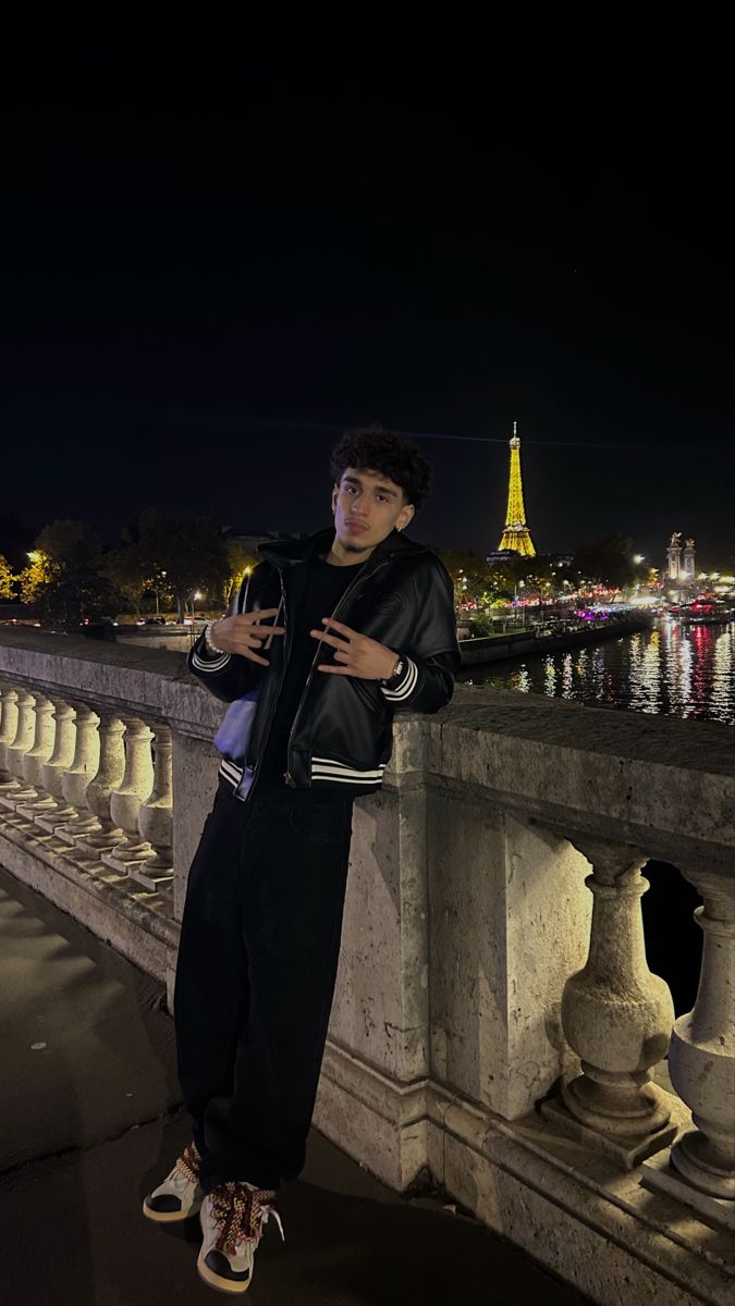 a young man standing on the edge of a bridge at night looking at his cell phone