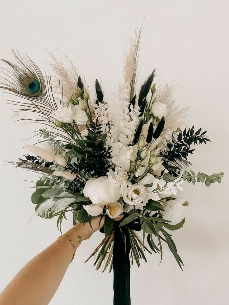 a person holding a bouquet with white flowers and feathers