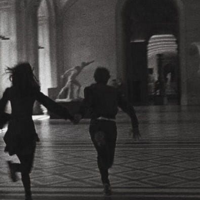 two people running through a building with statues in the background