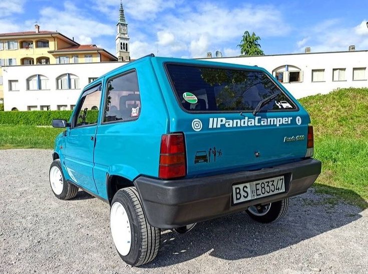 a small blue car parked on the side of a road in front of a building