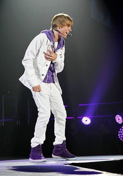 a male in a white suit and purple shoes is on stage with his hands together