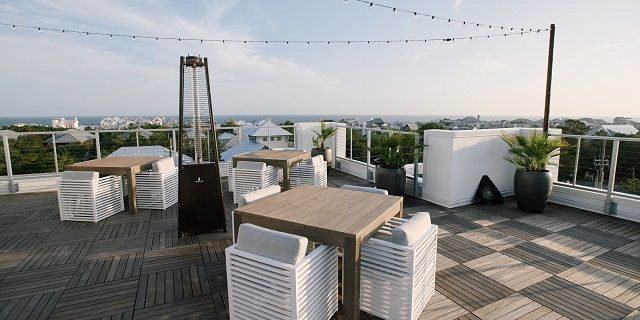 an outdoor dining area overlooking the ocean with white chairs and wooden tables set up for two