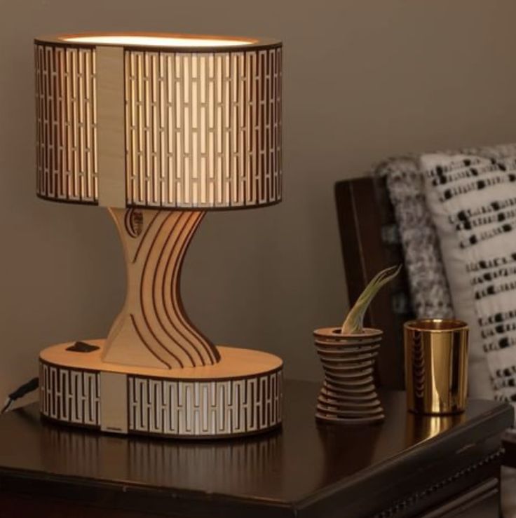 a lamp sitting on top of a wooden table next to a cup and gold vase