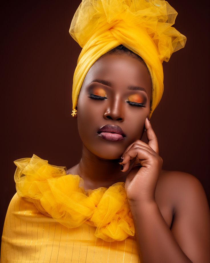 a woman wearing a yellow turban and holding her hand to her ear, posing for the camera