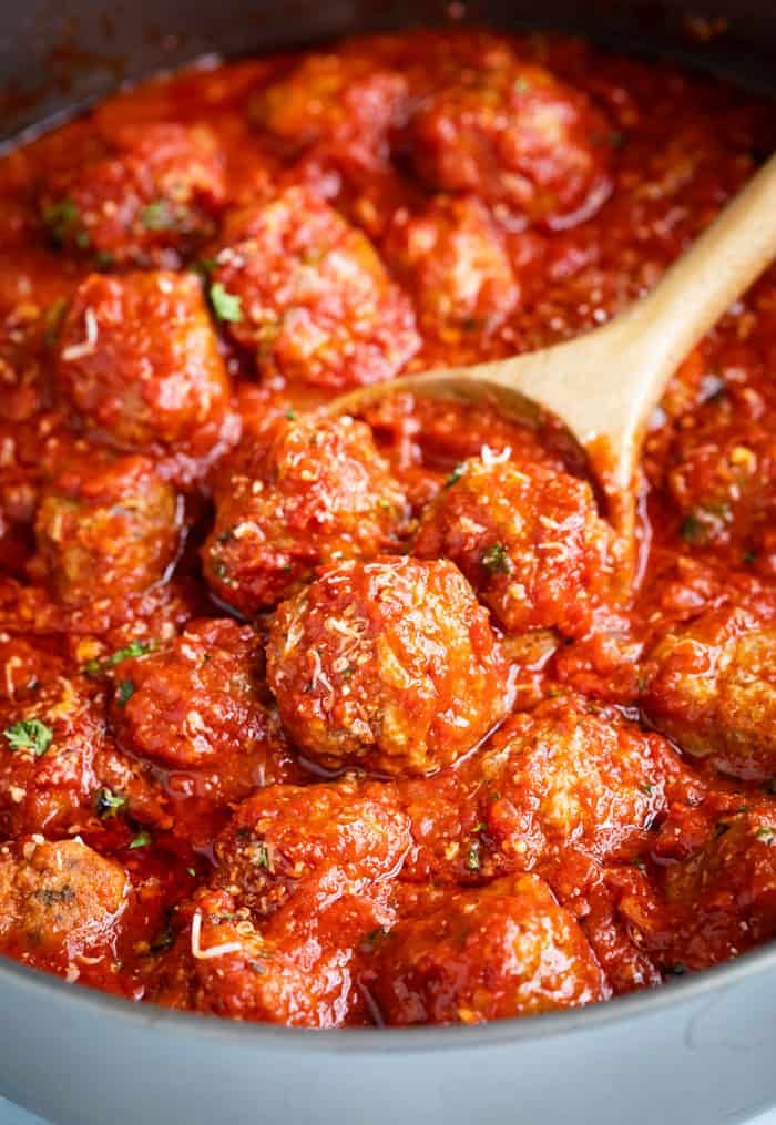 a wooden spoon in a pot filled with meatballs and marinara sauce on the stove