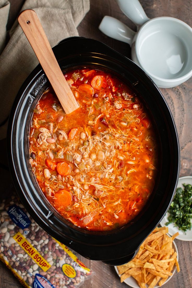 a crock pot filled with chicken and bean soup next to some chips on the side