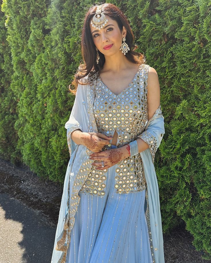 a woman in a blue dress standing next to some bushes