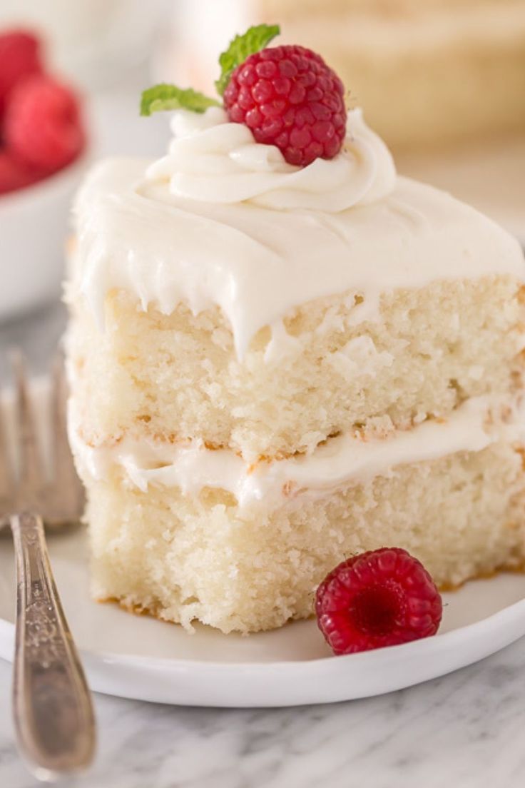 a piece of cake with white frosting and raspberries on the plate next to it