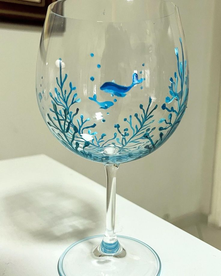 a wine glass with blue seaweed painted on the bottom and inside is sitting on a table