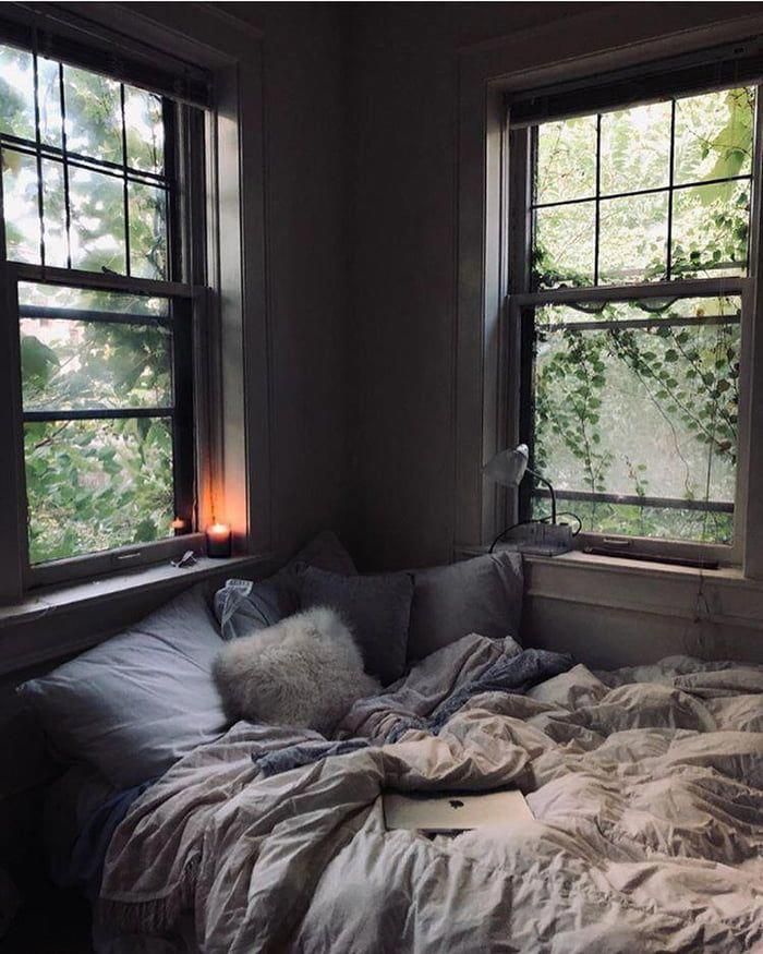 an unmade bed sitting in front of two windows