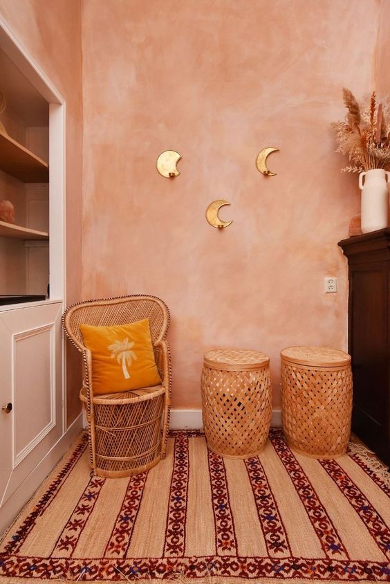 two wicker stools sit in front of a pink wall with gold sconces