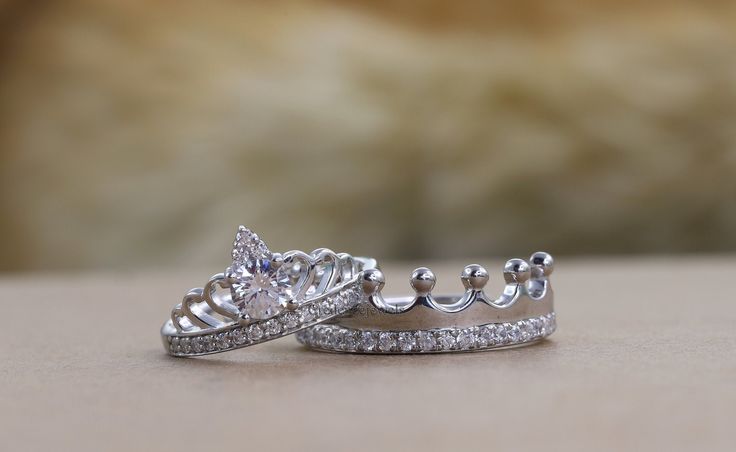 two wedding rings with diamond crowns on them sitting on a table next to each other