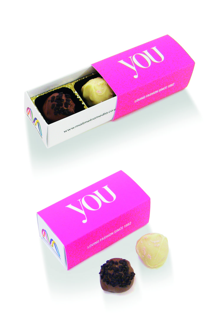 two chocolates in a pink box with the word you printed on it and an apple next to them