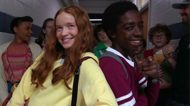 a group of young people standing next to each other in a hallway with one girl smiling at the camera