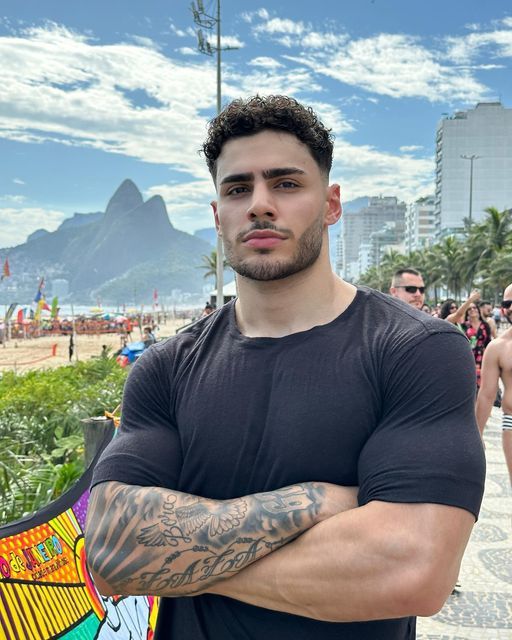 a man standing with his arms crossed in front of the camera and people on the beach behind him