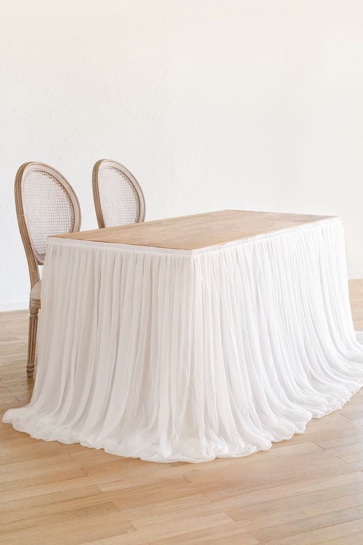 a table with two chairs and a white cloth draped over it on top of a hard wood floor