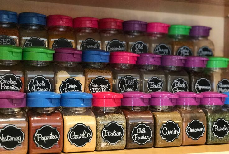 many different colored spices are stacked on the shelf in front of each other and labeled with labels