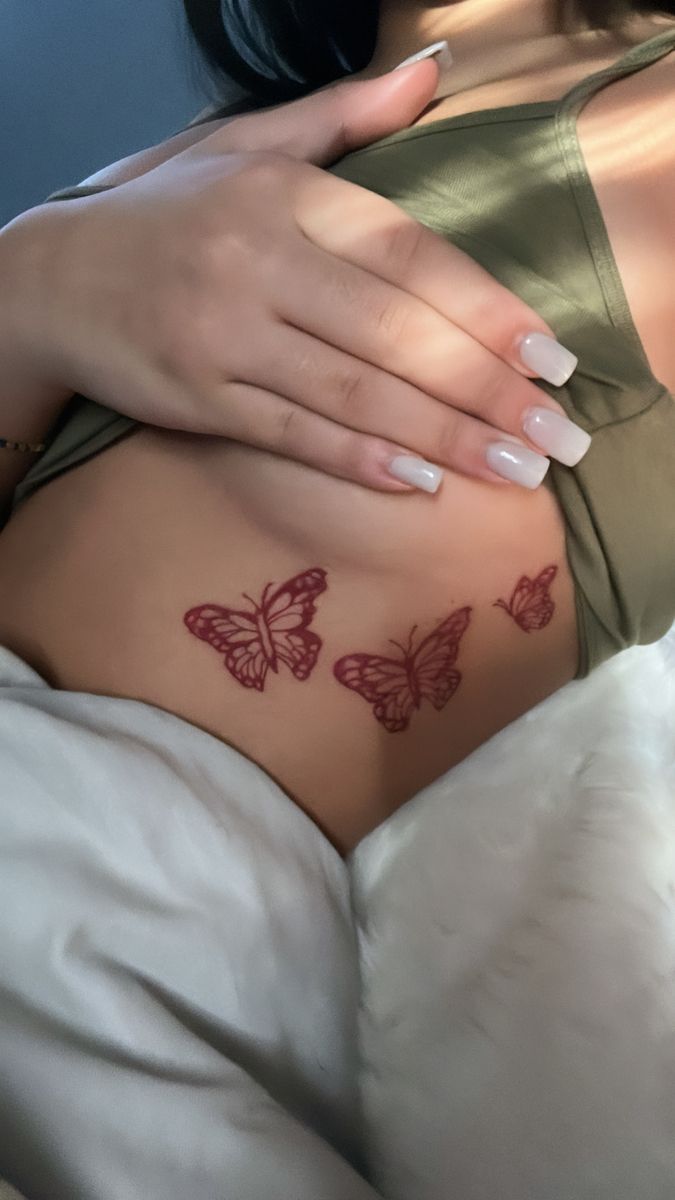 a woman's stomach with three butterflies tattooed on the side and her left breast