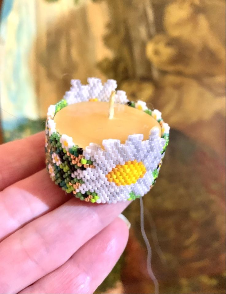 a hand holding a small beaded candle in the shape of a pineapple on it