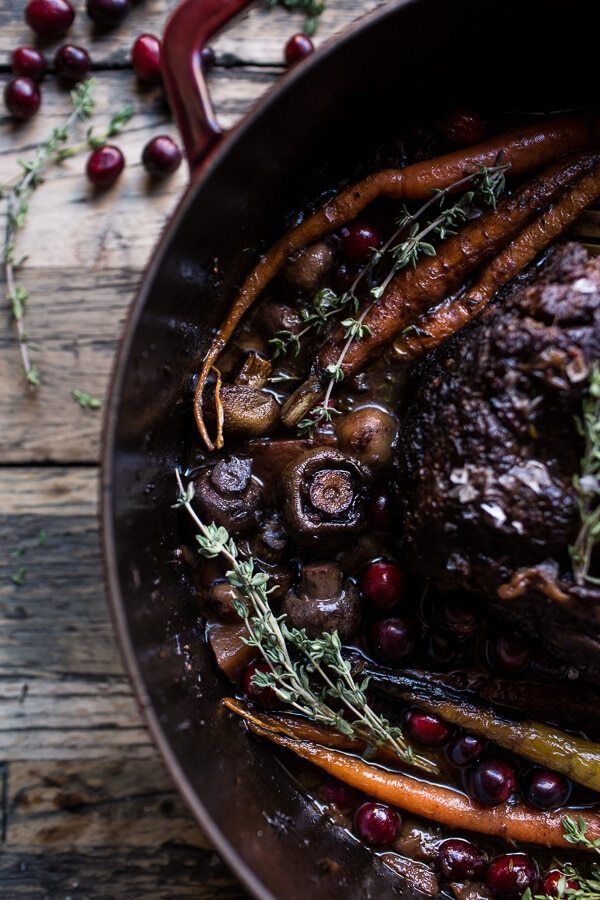 a pot filled with meat, carrots and cranberries on top of a wooden table