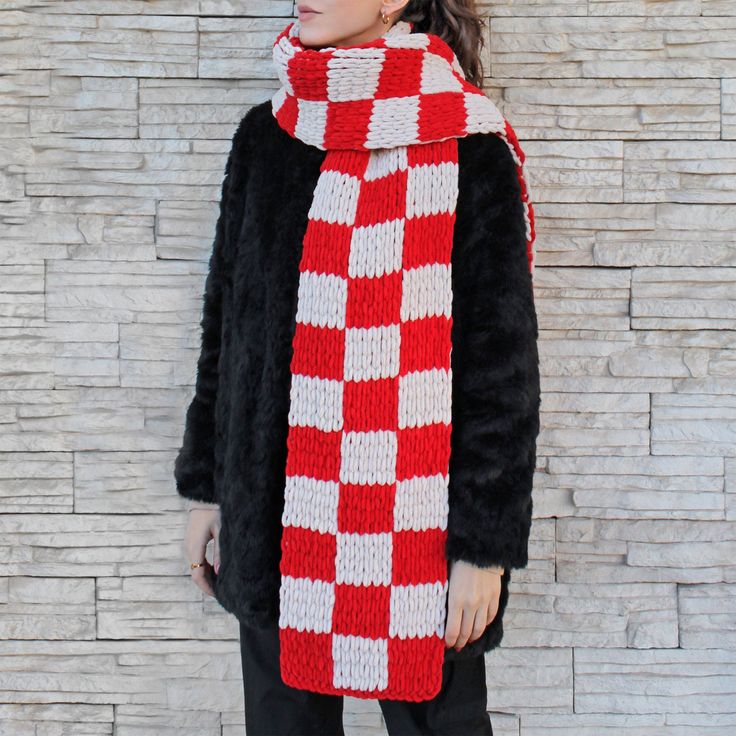 a woman standing in front of a brick wall wearing a red and white knitted scarf