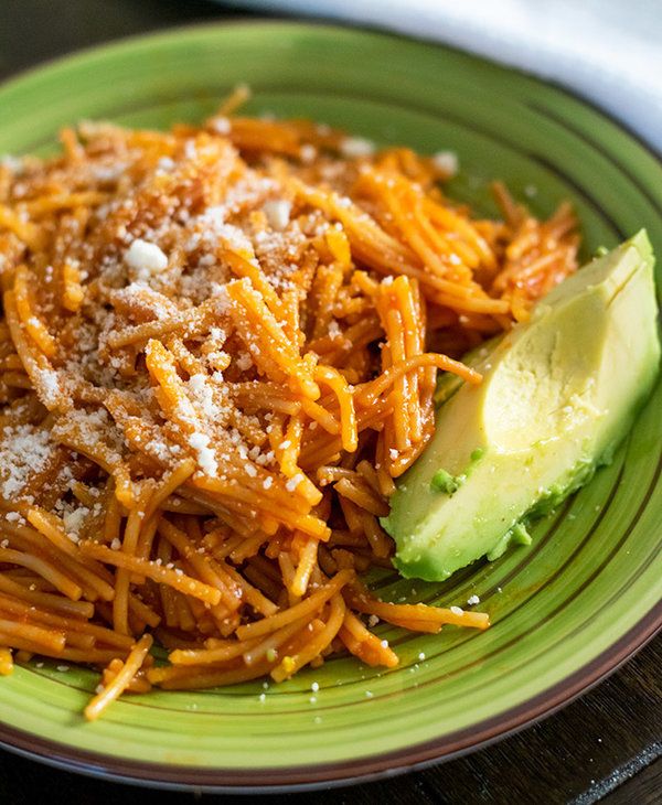 a green plate topped with spaghetti and an avocado wedged in the side