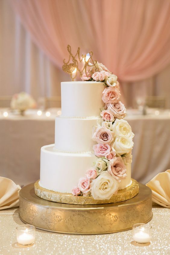 a three tiered wedding cake with pink and white flowers on the top is surrounded by candles