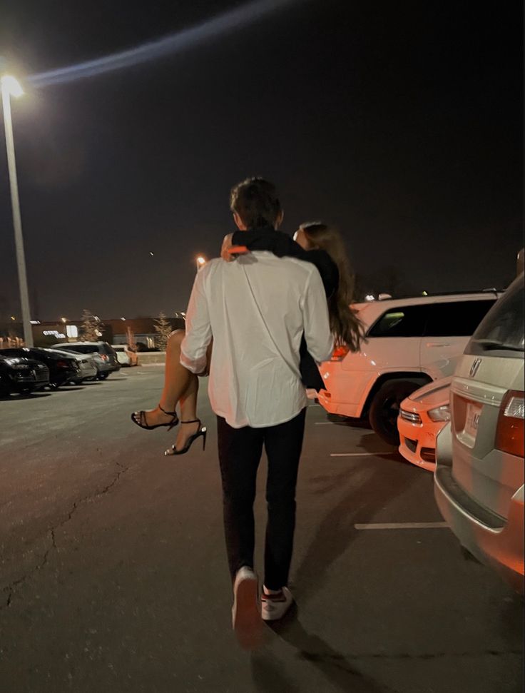 a man and woman are walking in the parking lot at night with their arms around each other