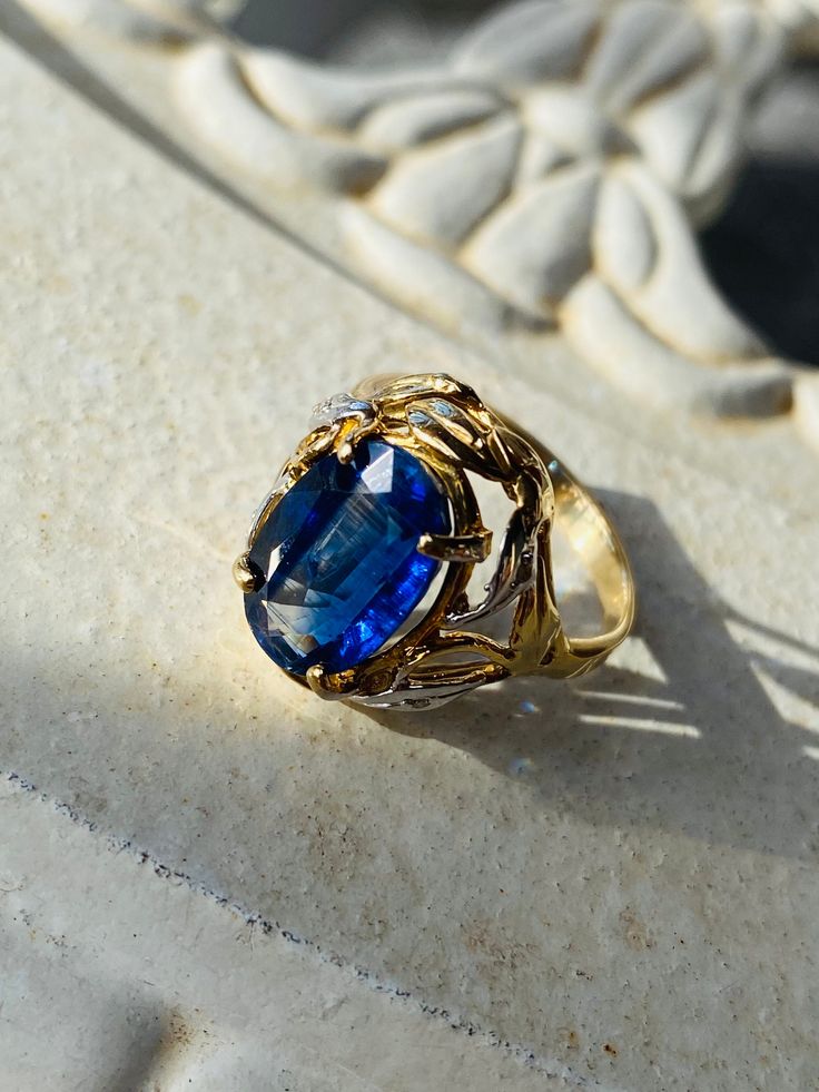 Imagine the deepest royal blue colour in an oval cut kyanite nestled in a bed of flora, namely leaves in a two tone 14k white and yellow gold setting scattered with diamonds in a raised filigree frame as it's adornment design. This blue beauty does not go unnoticed at 2.60 carats in stone weight and measuring 12.50mm x 8.40mm x 4mm deep with four leaves surrounding and encased with one diamond of .005 points, each single cut.  The hallmarks of a Kyanite gemstone resemble that of a sapphire visually however without the exuberant price and only a trained eye could tell the particular differences. This ring has cathedral style workmanship paying homage to the Arts & Crafts era of jewellery design.  The shank is 2.20mm wide, tapered up to 2mm wide with a flat profile. The setting width being 1 Royal Blue Colour, Filigree Frame, Blue Beauty, Deep Royal Blue, Arts Crafts Style, Gold Cocktail Ring, Golden Jewelry, Gold Cocktail, Dream Engagement