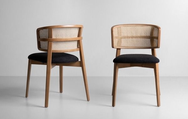 two chairs sitting side by side in front of a white wall and one has a black cushion on it