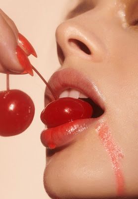 a woman with red lipstick and cherry on her lip is holding a stick to the cherries