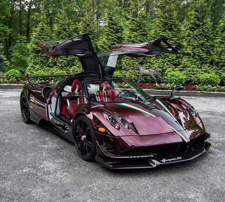 a red sports car with its doors open in a parking lot next to some trees