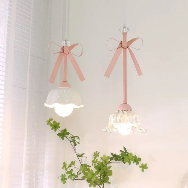 two hanging lights with bows on them hang from the ceiling above a plant in a vase