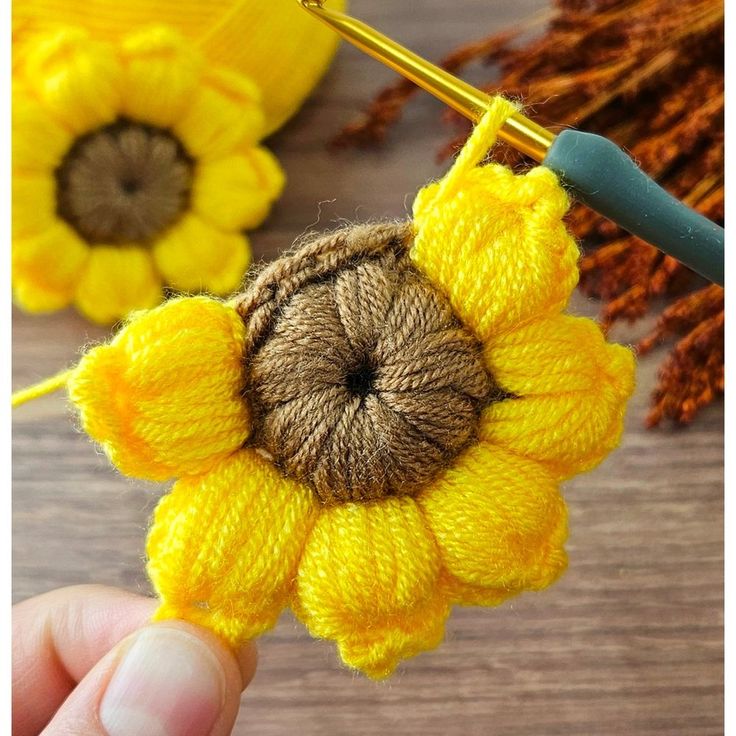 a person holding a needle and thread with a yellow flower on the end of it