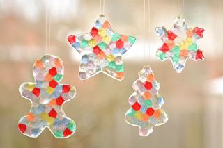 three glass ornaments hanging from strings in the shape of stars and christmas trees on a window sill