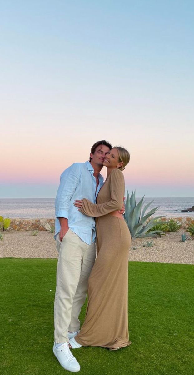 a man and woman kissing in front of the ocean at sunset with an agamal behind them